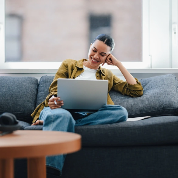 Person using a laptop while relaxing at home, representing convenient saving and online account access.