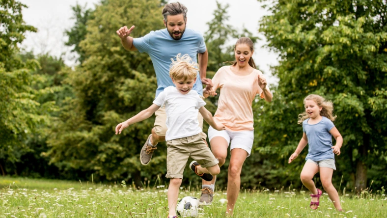 Group of adults and children playing soccer together in a grassy park.