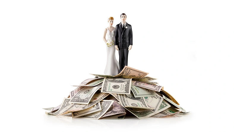 Bride and groom figurines standing on a pile of cash representing a wedding cash registry or monetary gifts.
