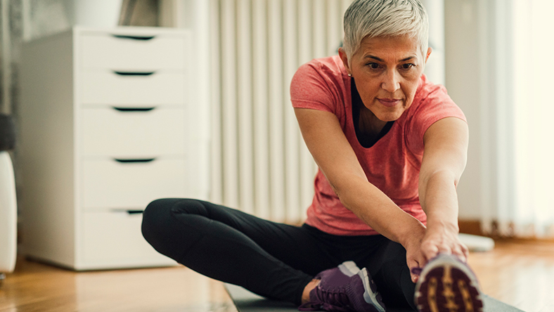 Mature woman stretching leg on floor.