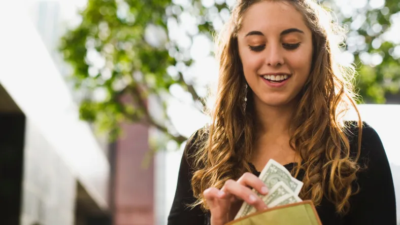 Person taking cash out of a wallet while standing outdoors.