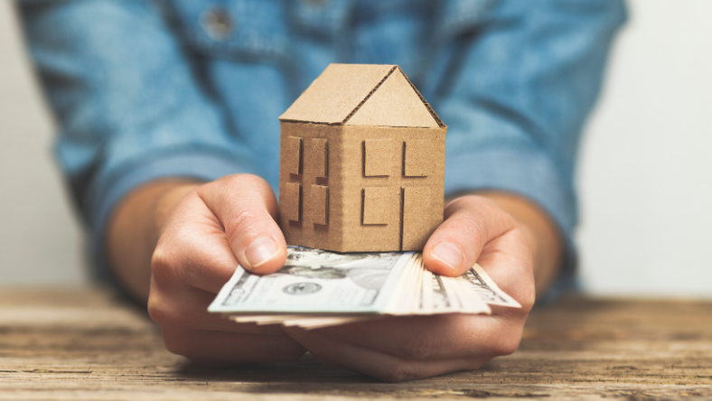 Hands holding cash and model of a home.