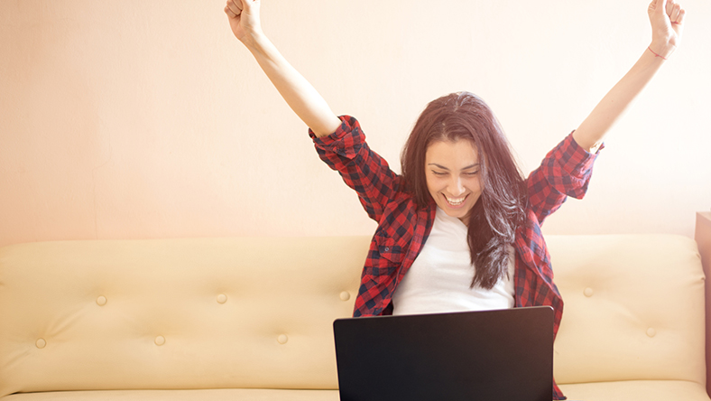 Woman raising her arms and smiling down at her laptop.