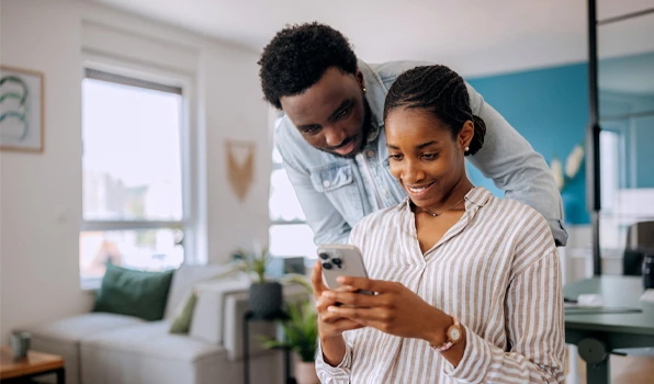Two people reviewing account information on a smartphone in a home setting, illustrating convenient digital banking and mobile account management.
