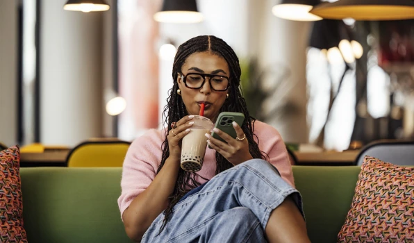 Person using a smartphone while relaxing with a drink, representing convenient checking account access and mobile banking from anywhere.