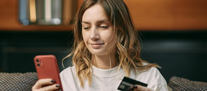 Happy woman looking at phone and holding debit card.