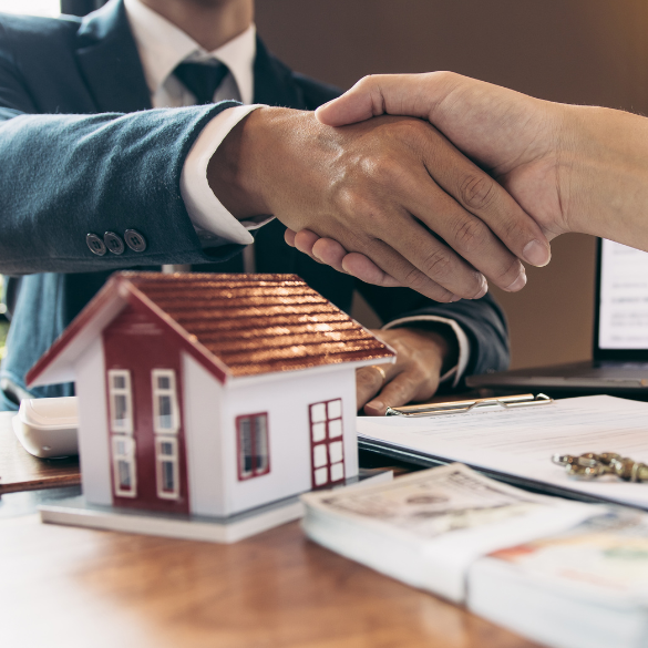 Handshake over a model home and cash displayed on table.