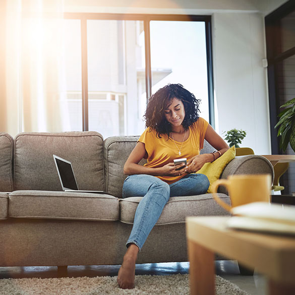 Woman casually sitting on couch using mobile phone and laptop.