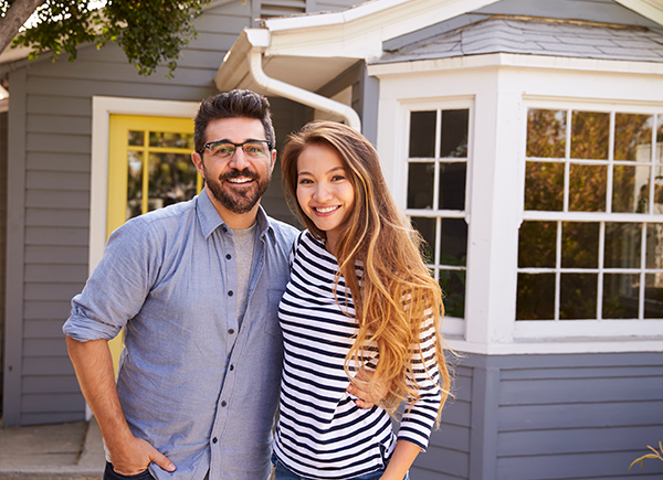 Young homeowners smiling in front of a home